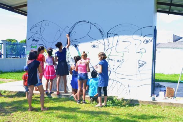 Crianças ajudando a fazer pintura em muro em bairro da periferia de Manaus.