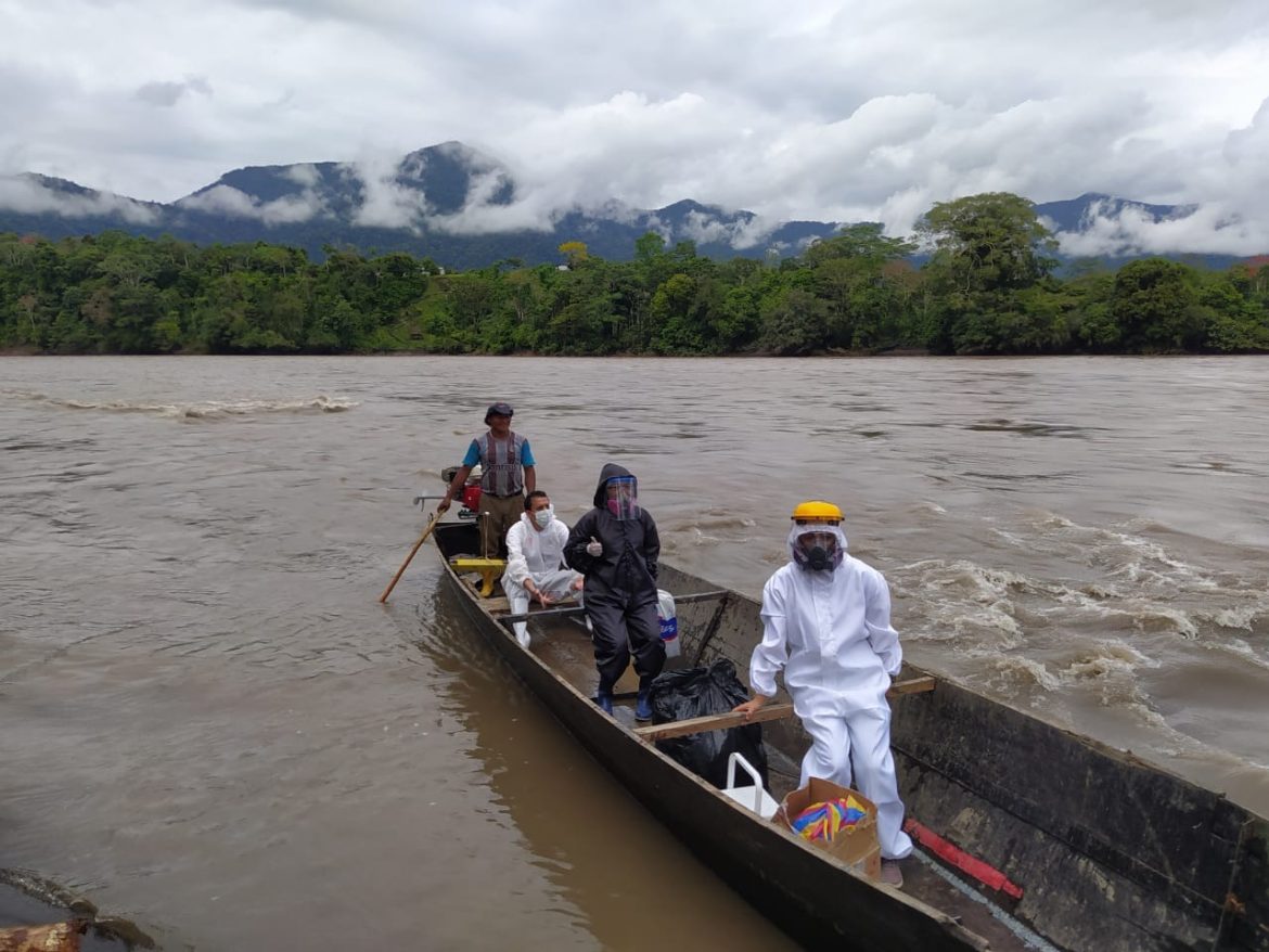 Pessoas com macacão de proteção contra a covid-19 em barco no meio do rio no Amazonas.