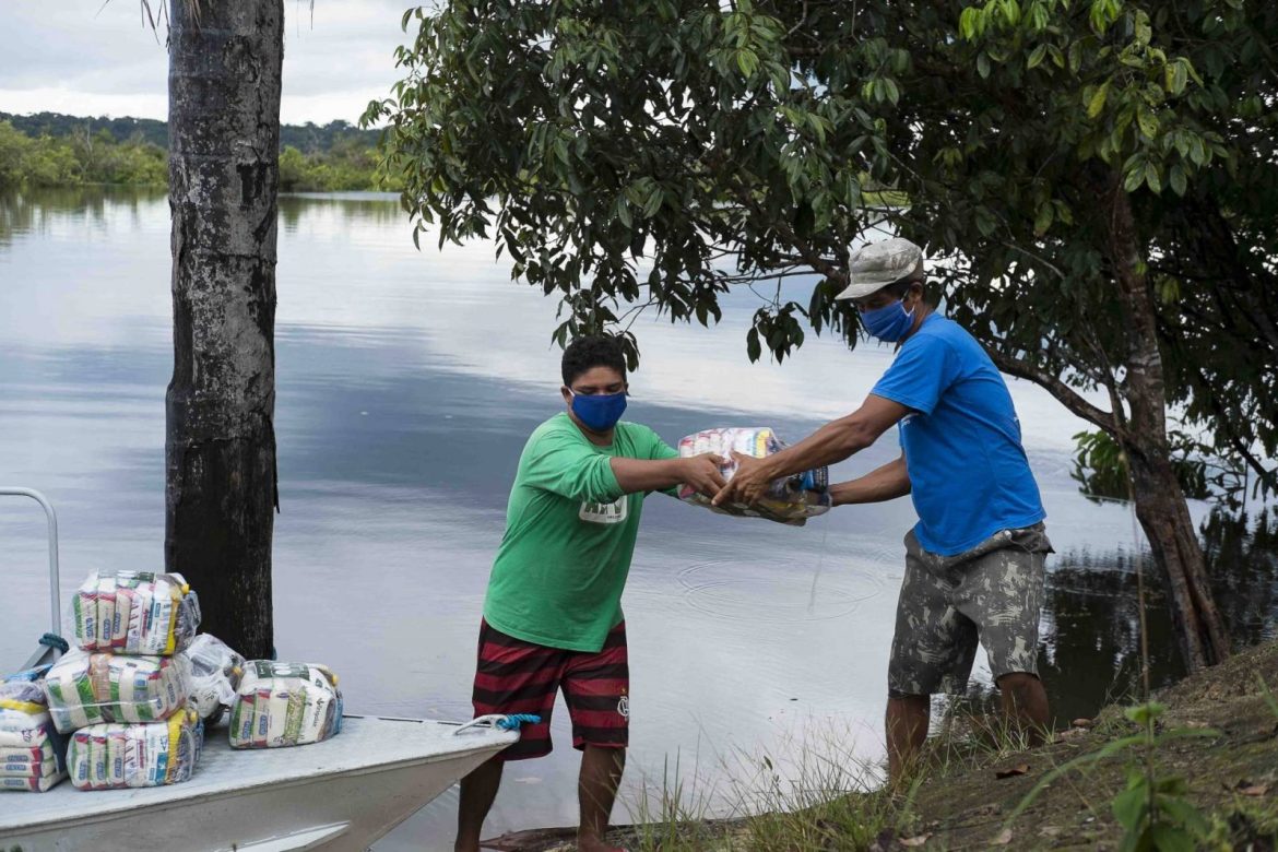 Homem entregando cestas básicas para moradores de comunidades ribeirinhas no interior do Amazonas.