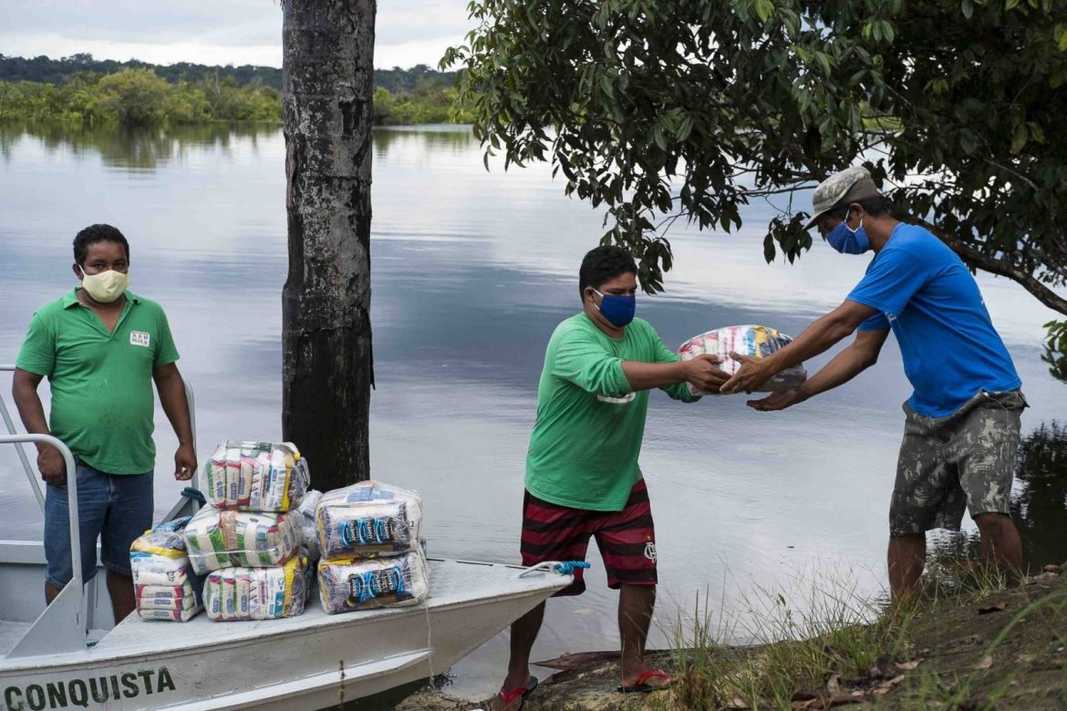 Homem entregando cestas básicas para moradores de comunidades ribeirinhas no interior do Amazonas.