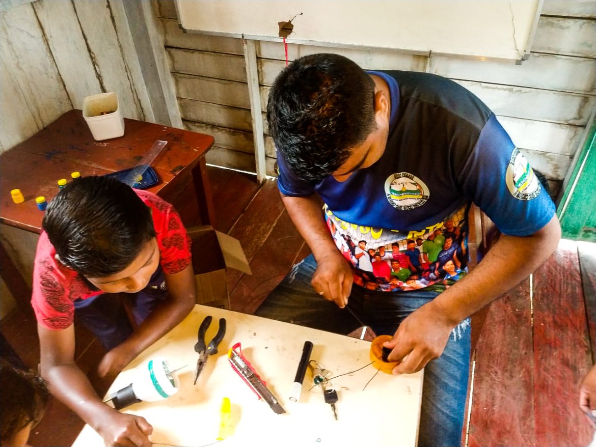 Professor fazendo trabalho manual com seus alunos em escola no interior do Amazonas.