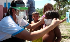 Mulher colocando máscara de proteção em criança ribeirinha, no interior do Amazonas.