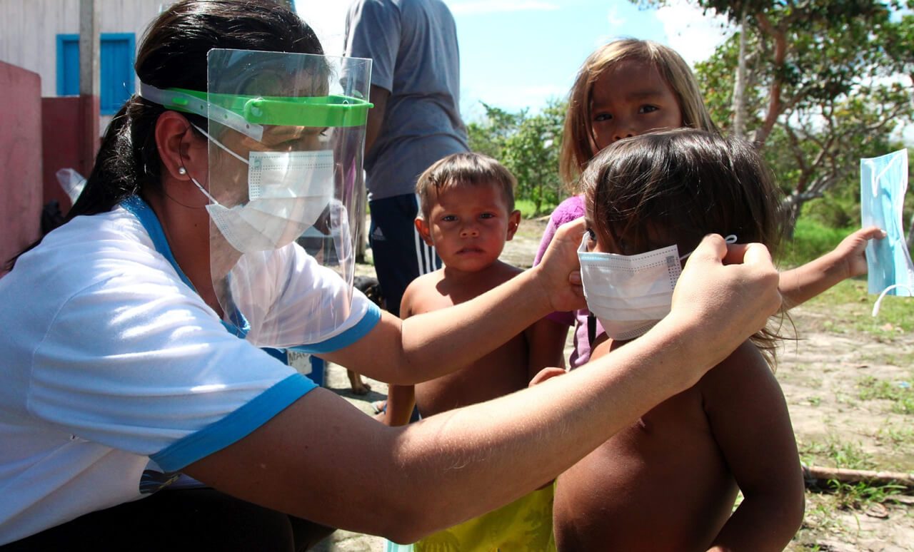 Mulher colocando máscara de proteção em criança ribeirinha, no interior do Amazonas.