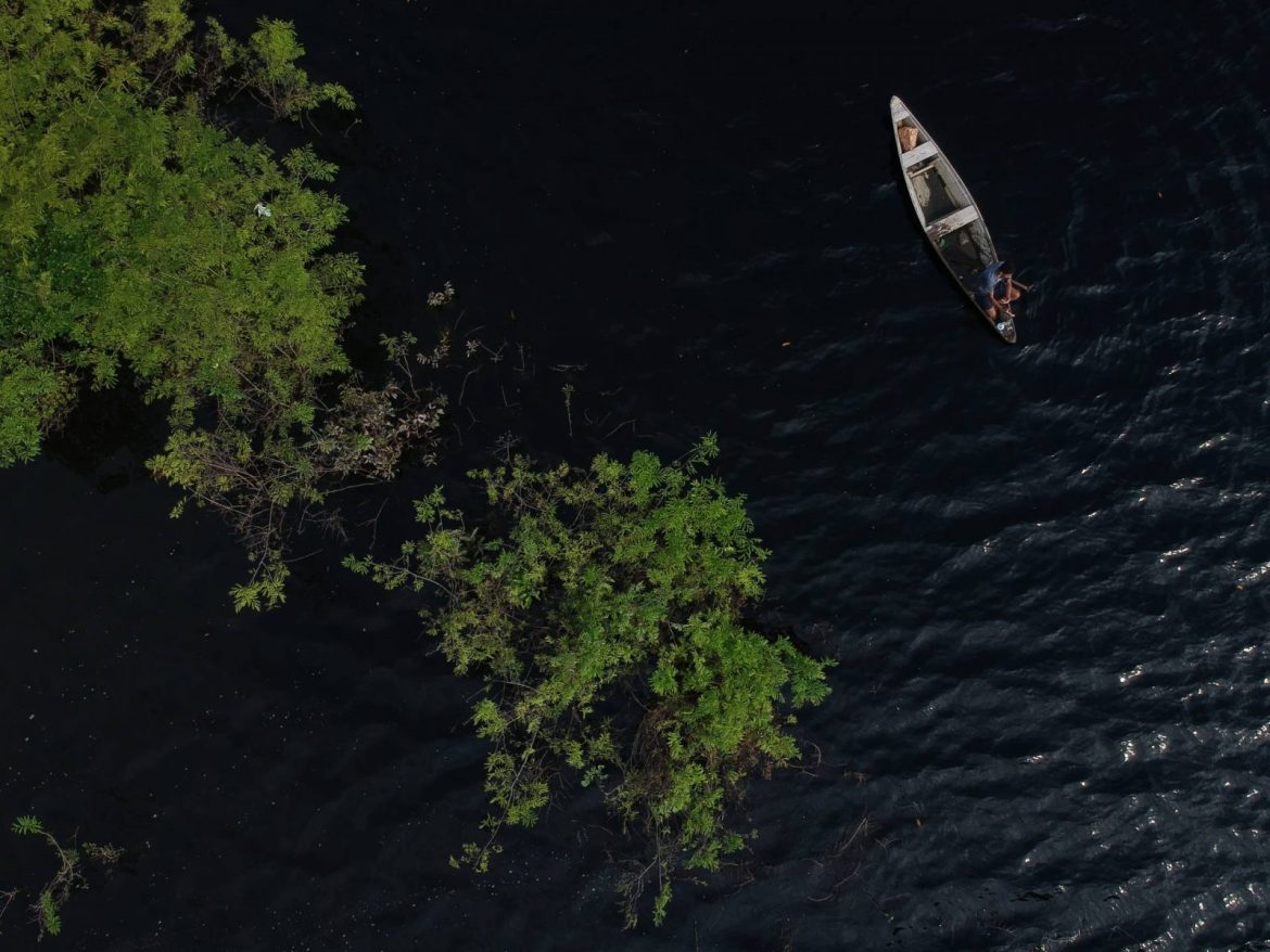 Ribeirinho em sua canoa navegando pelo rio negro no Amazonas.