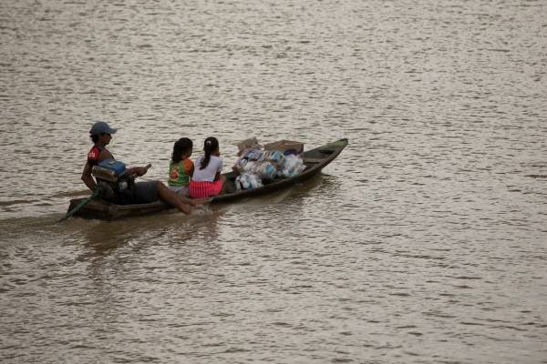 Homem pilotando barco, levando sua família e alimentos.