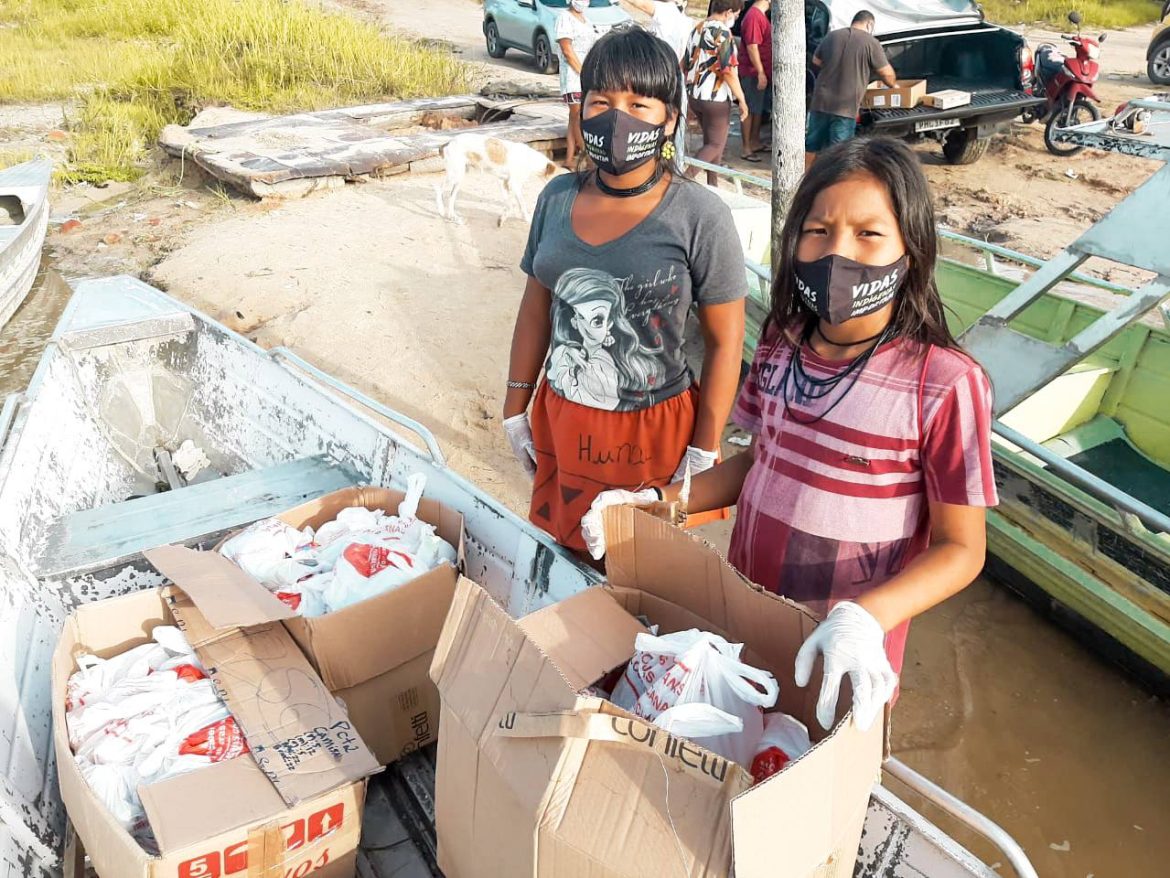 Mulheres indígenas recebendo doações de cestas básicas.