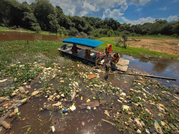 Pequena embarcação com pessoas coletando resíduos jogados em igarapé aos arredores de Manaus.