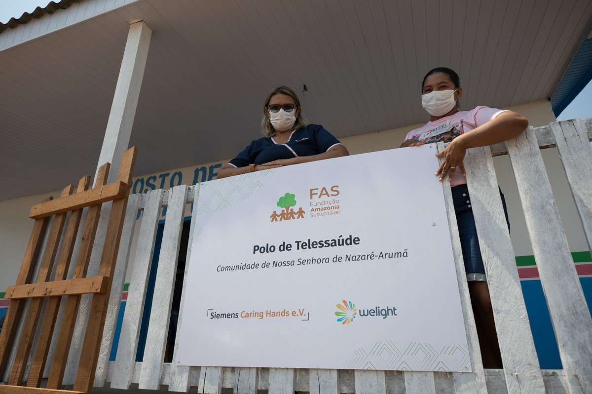Duas mulheres próximo a placa de polo de telessaúde, localizado na Comunidade de Nossa Senhora de Nazaré-Arumã, no interior do Amazonas.
