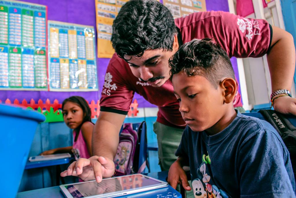 Tutor da Fundação Amazônia Sustentável (FAS), mostrando conteúdo no tablet para criança em sala de aula.
