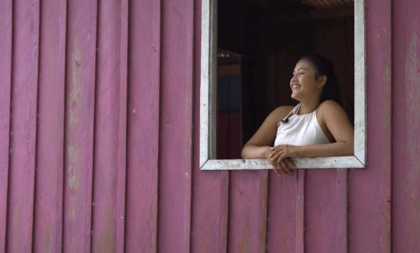 Jovem indígena sorrindo, na janela de sua casa na comunidade Três Unidos no Amazonas.