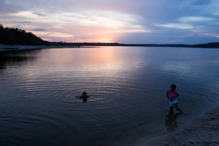 Crianças nadando no rio em pleno pôr do sol.