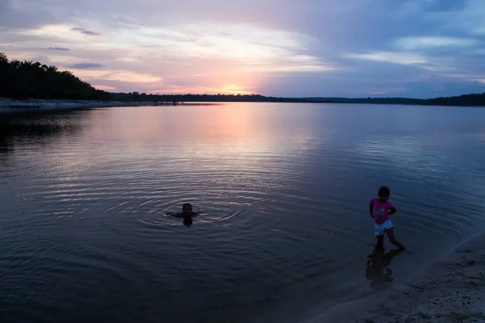 Crianças nadando no rio em pleno pôr do sol.
