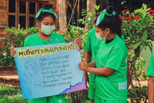 Duas meninas ribeirinhas segurando cartaz em atividade do projeto Deixa a mana Jogar, realizado pela Fundação Amazônia Sustentável (FAS).