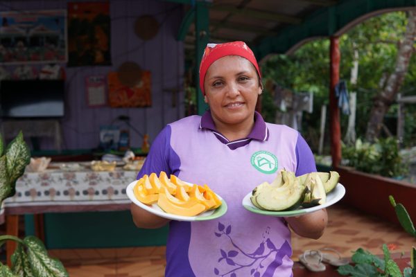 Mulher indígena segurando um prato de frutas em frente a sua pousada, localizada na comunidade Três Unidos, no interior do Amazonas.