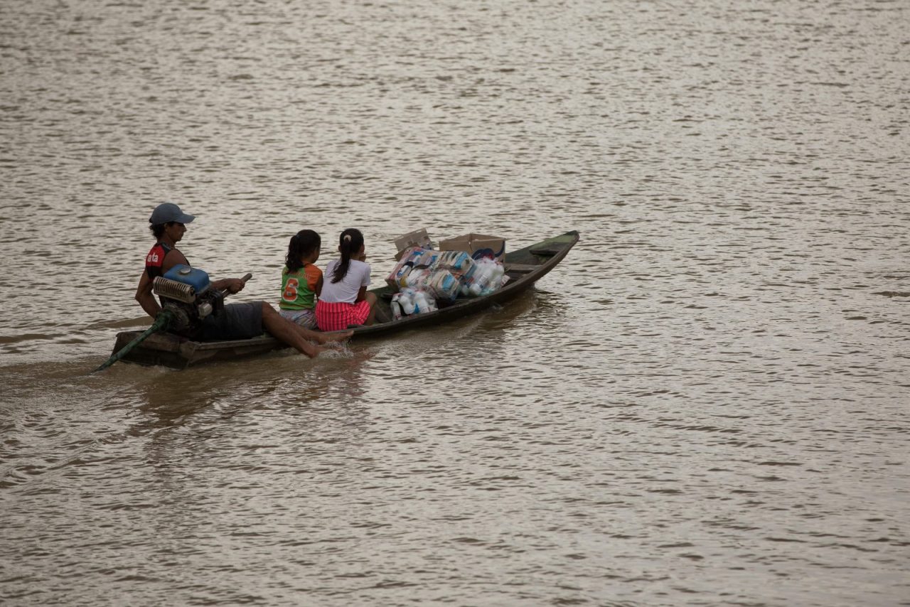 Pessoas em canoa levando cestas básicas para sua comunidade.