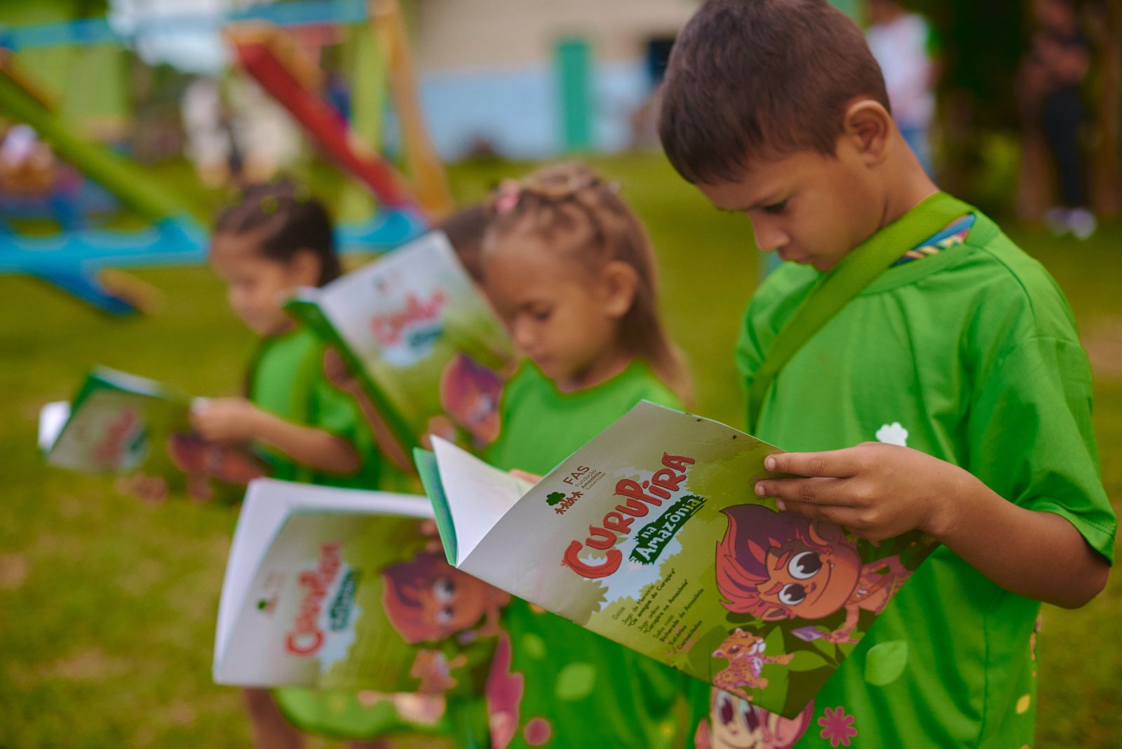 Crianças segurando livro criado pela Fundação Amazônia Sustentável (FAS) sobre educação.