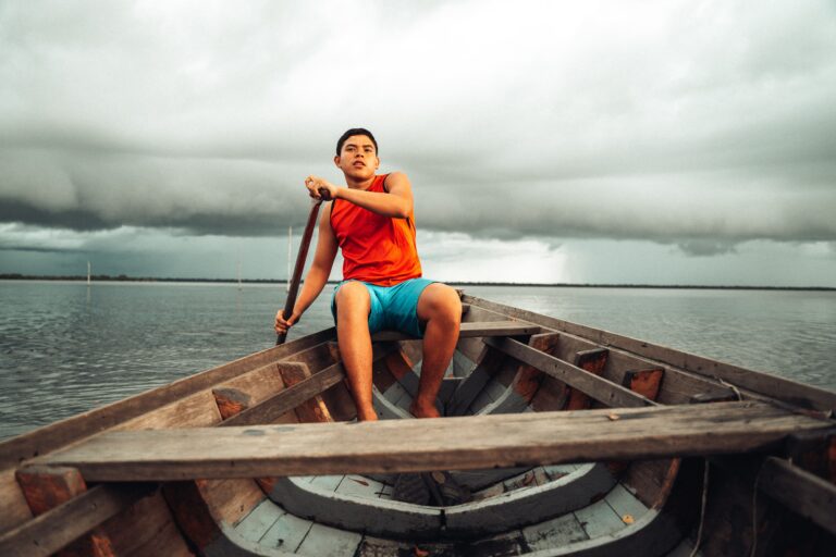 Garoto em canoa remando em meio ao Rio Negro.