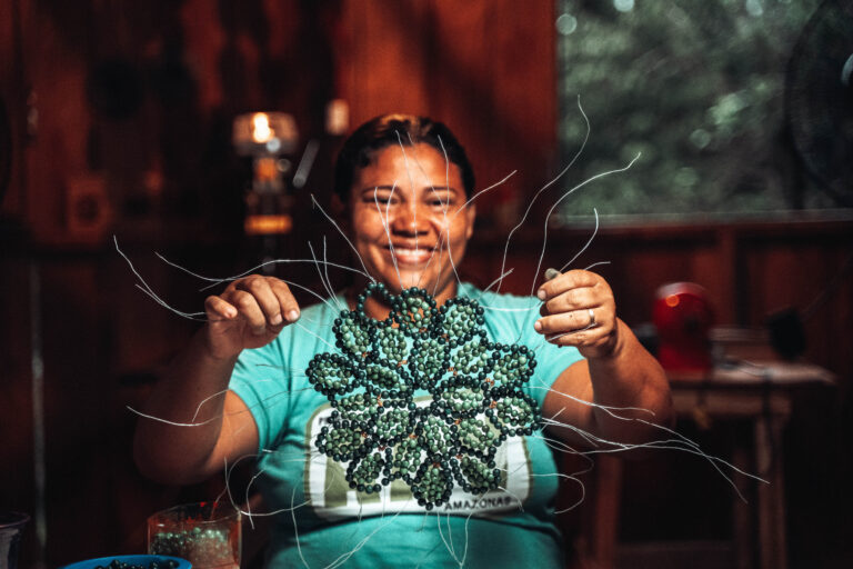 Mulher segurando artesanato produzido manualmente com sementes de frutos da Amazônia.