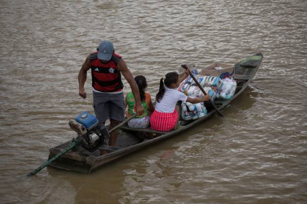 Duas crianças e um homem na canoa, navegando pelo rio Amazonas.